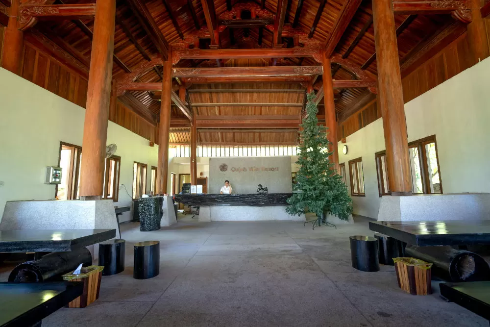 Open-air resort lobby with carved timber beams and a stone reception desk, a Christmas tree beside it.